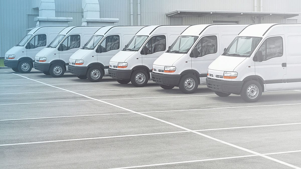 Six white vans neatly parked behind a warehouse parking lot
